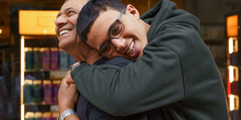 Senior Father And Son Hugging On The Mall. Hug for dad. A teen boy leans over to hug his father, who to be smiling at him.